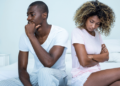 Unhappy black couple seated on bed - tolerable level of permanent unhappiness
